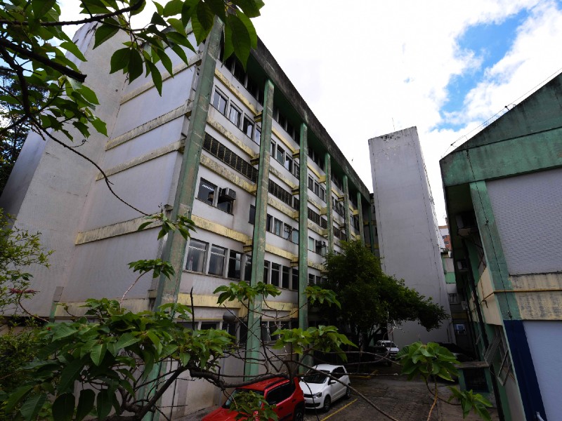Foto do prédio onde funciona o HM Waldomiro de Paula. Do lado esquerdo há um prédio com seis pavimentos, ao fundo um outro prédio e do lado direito mais uma parte do hospital. Há três carros estacionados e algumas árvores